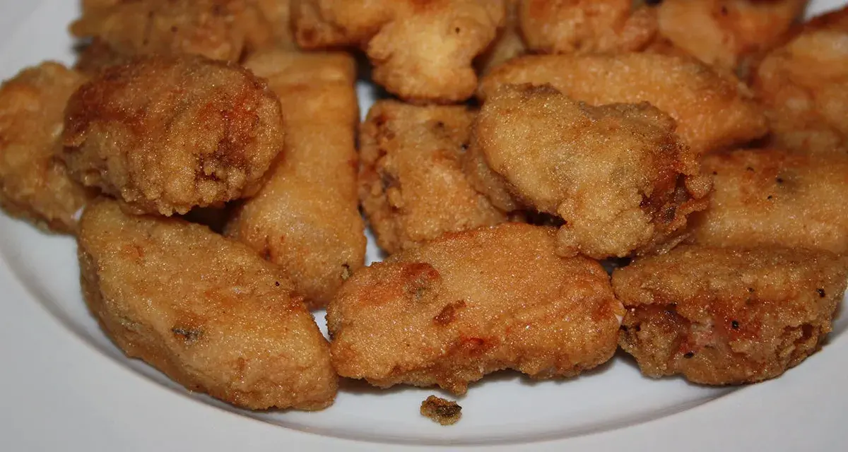 Un plato blanco lleno de trozos dorados y crujientes de japuta en adobo, listos para disfrutar.