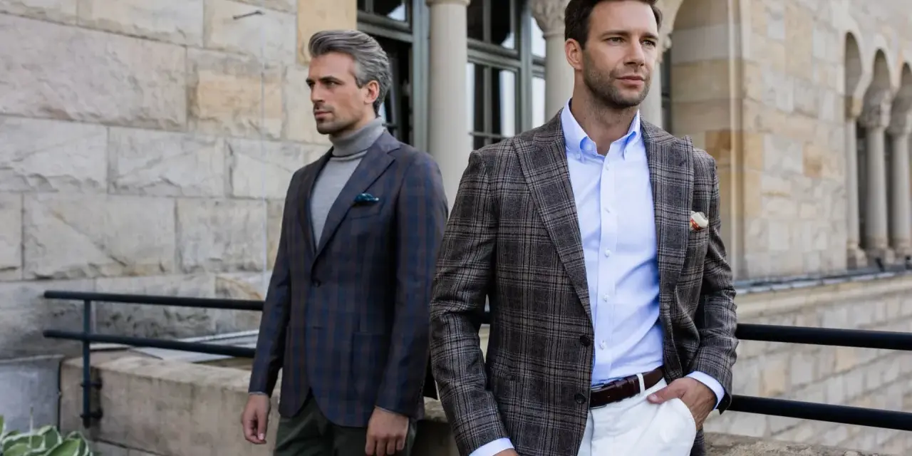 Dwóch eleganckich mężczyzn w marynarkach w kratę. Jeden ma szary golf, drugi błękitną koszulę. Stylowy mankiet co to?