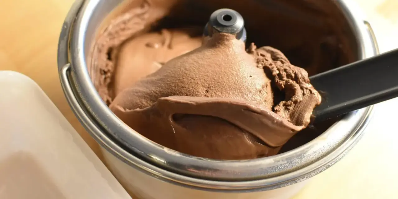 Un cucchiaio nero preleva una porzione di cremoso gelato fatto in casa al cioccolato da una gelatiera.