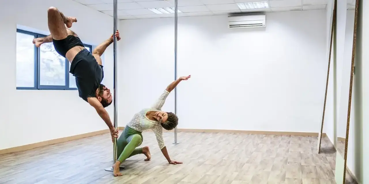Para ćwiczy pole dance, pokazując efekty odchudzania. On wisi na rurze, ona kuca obok.