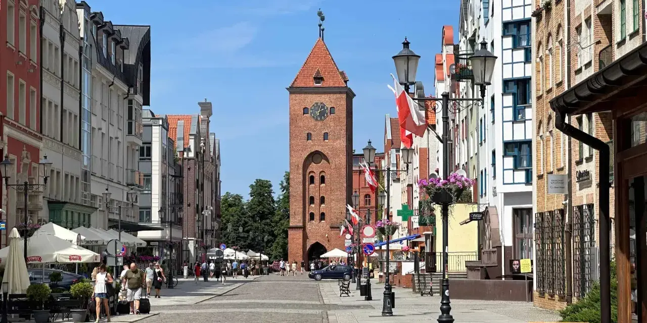 Ulica w Elblągu, z charakterystyczną wieżą i kolorowymi kamienicami. To najniżej położone miasto w Polsce, pełne urokliwych zakątków.