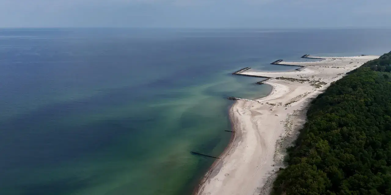 Plaża w Jarosławcu, zwana czasem "plażą dubaj", z kamiennymi falochronami i zielonym lasem.