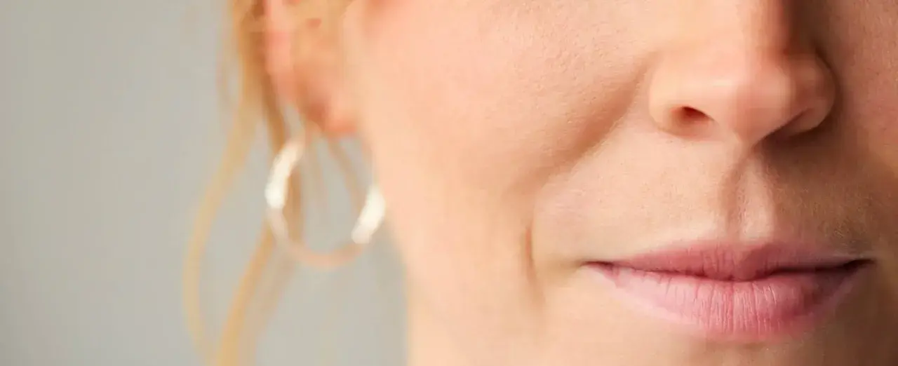 Nahaufnahme eines Gesichts mit sichtbarer Nasolabialfalte, die mit 40 Jahren typisch ist. Eine Frau mit dezentem Lächeln.