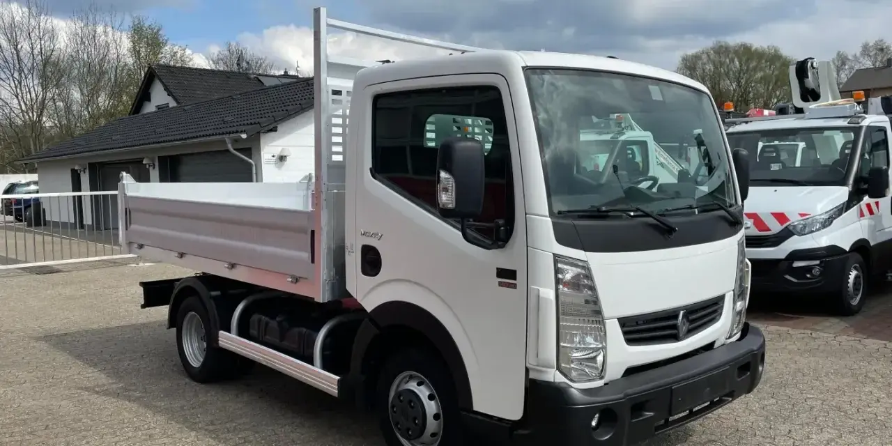 Biały Renault Maxity z otwartą skrzynią ładunkową stoi na placu. W tle budynek i inne pojazdy.