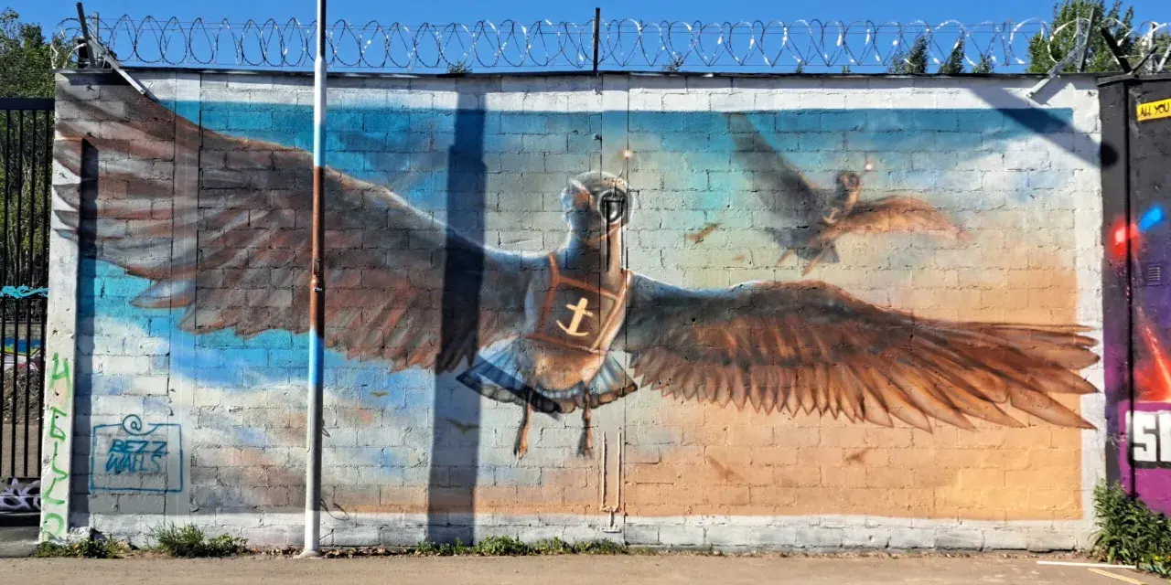 Street art i Stockholm: en stor målad fågel med utbredda vingar, som flyger mot en blå himmel.