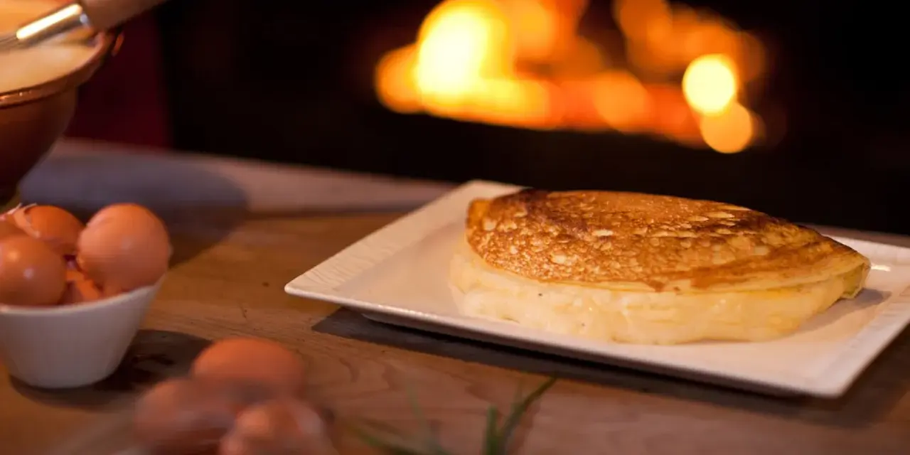 Une omelette mere poulard dorée et moelleuse, prête à être dégustée près d'un feu de cheminée. Des œufs frais sont visibles à côté.