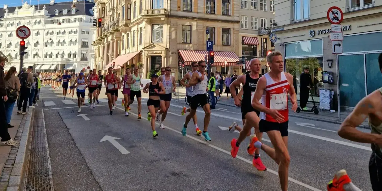 Corredores compiten en una media maratón en Europa, con edificios históricos y público animando.