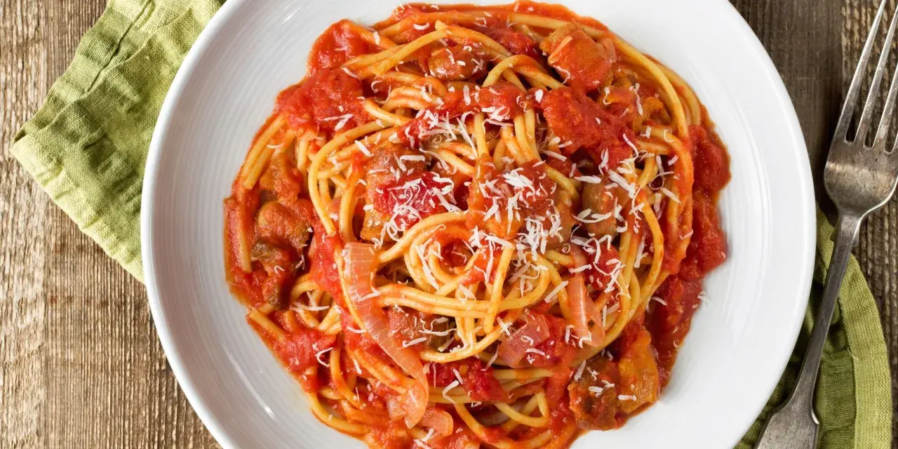 Spaghetti al pomodoro con pezzi di carne e cipolla, uno dei classici sughi per pasta, spolverati di parmigiano.