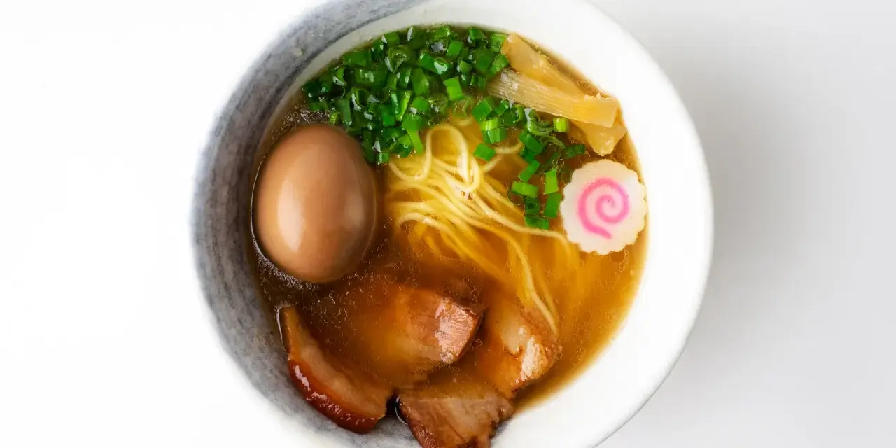A miseczce shoyu ramen z makaronem, jajkiem, plastrami wieprzowiny, szczypiorkiem, bambusem i różową rybną kluską.