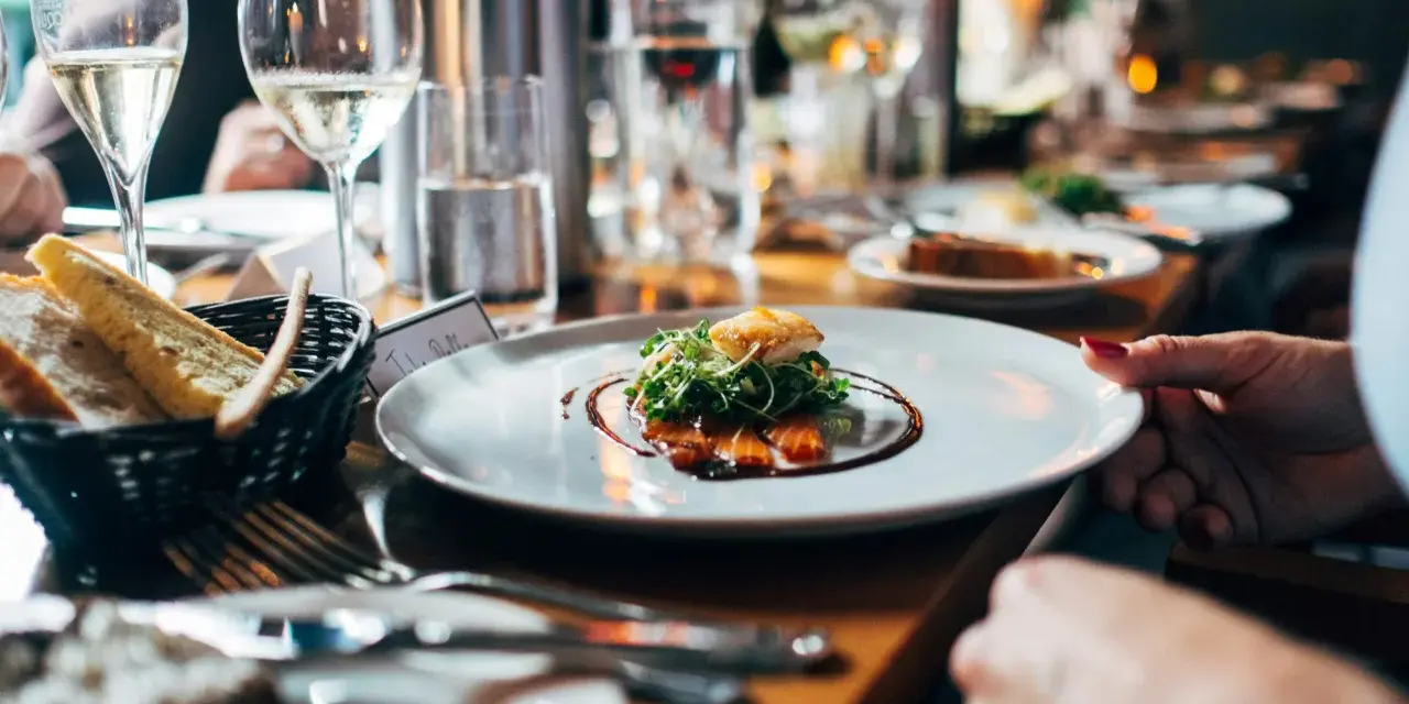 Un plato con salmón y brotes verdes, pan en una cesta y copas de vino. Una experiencia gastronómica que celebra un menú sostenible.