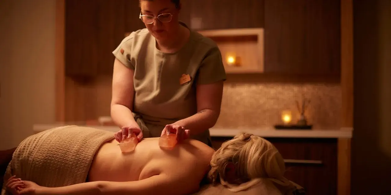 A therapist performs a Himalayan salt massage, placing warm salt stones on a client's back.
