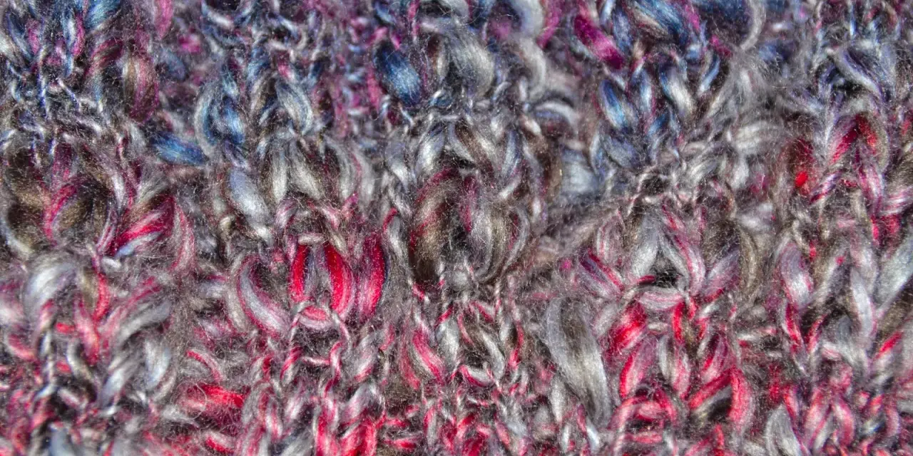 Detaljerad vy av en stickad tubhalsduk i garn med färger som grått, rosa och blått. Mönstret är en enkel slätstickning.
