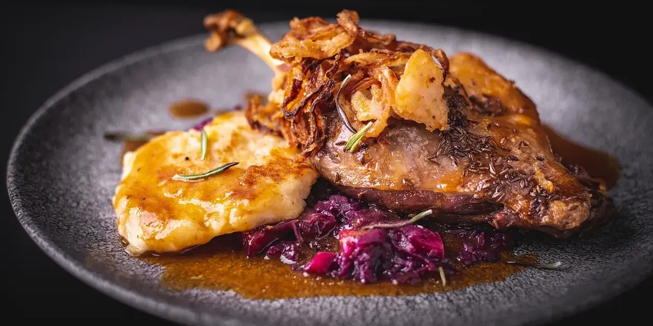Pieczona kaczka z chrupiącą cebulką, purée i czerwoną kapustą na talerzu.