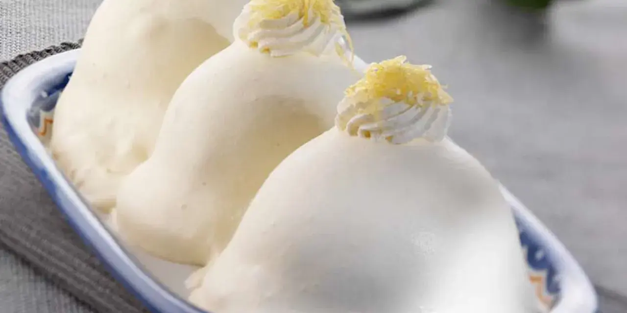 Tre deliziose delizie al limone, guarnite con panna e scorza di limone, in un piatto blu e bianco.