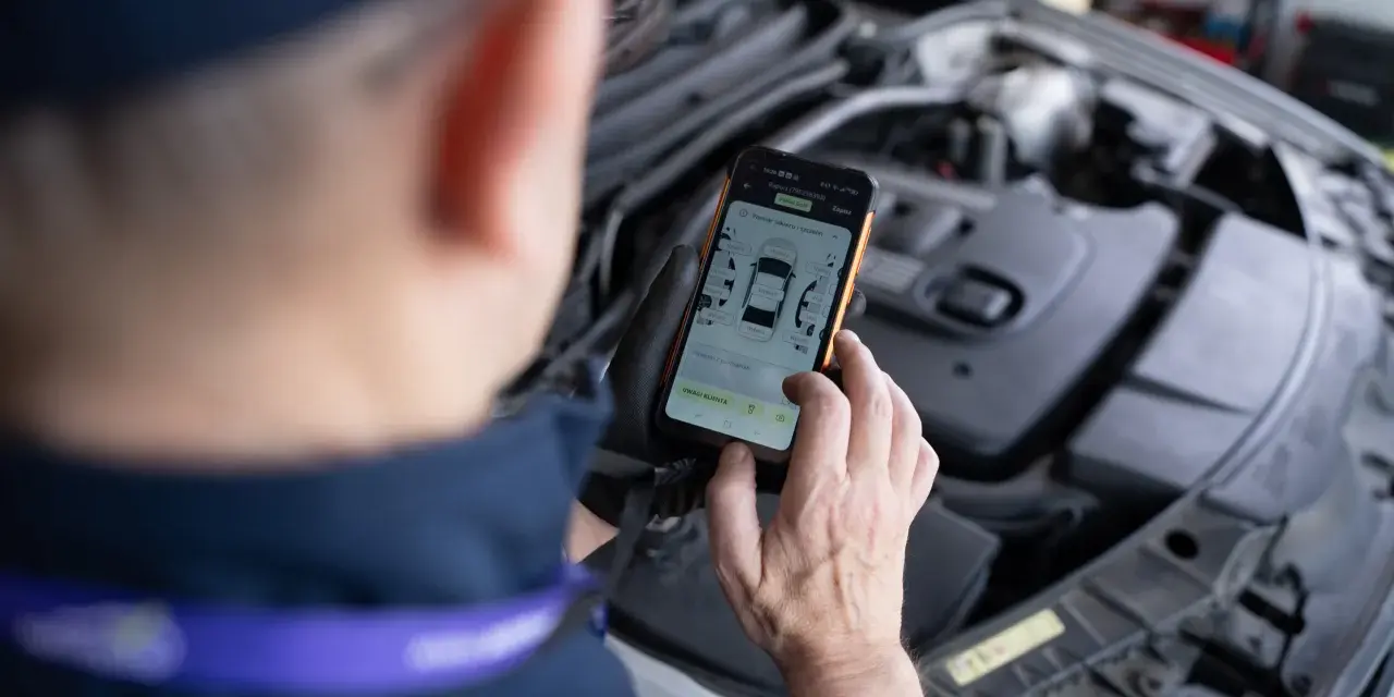 Mechanik sprawdza kody błędów DTC Renault na telefonie, analizując raport z pomiaru lakieru.