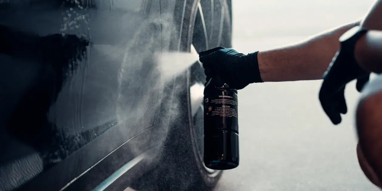En hand med handske sprayar en bil för att ta bort dekaler.