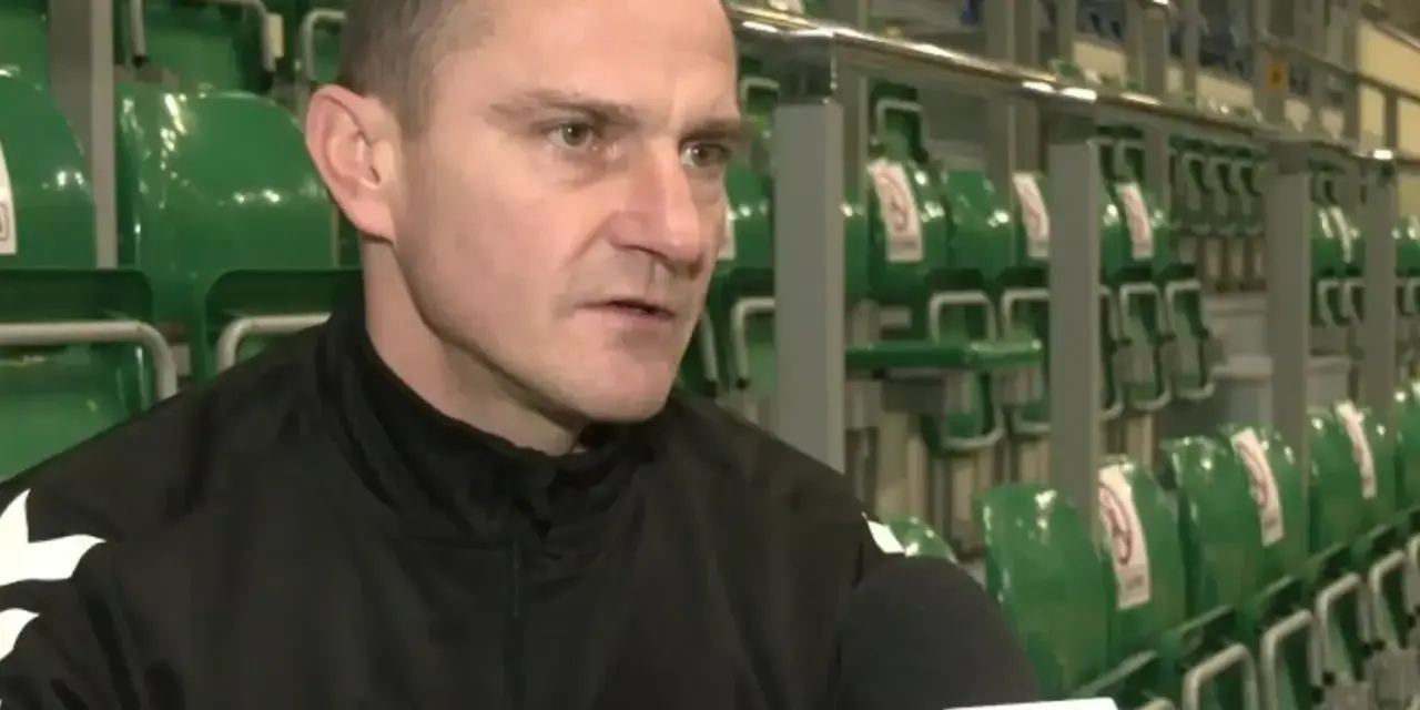 Marcin Pilch udziela wywiadu przed rzędem zielonych krzesełek na trybunach.