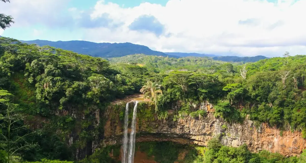Majestatyczny wodospad na Mauritiusie spada kaskadami po skalnej ścianie, otoczony bujną, zieloną dżunglą i górami w tle.