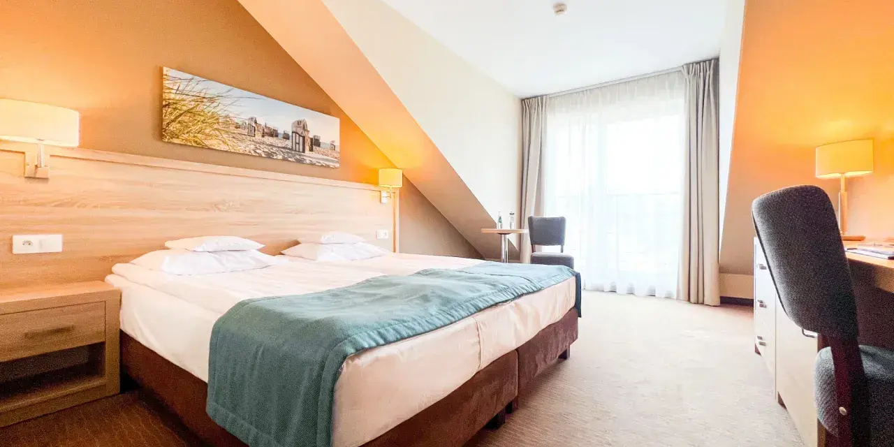Przytulny pokój hotelowy z wygodnym łóżkiem, biurkiem i oknem. Idealne miejsce na nocleg tranzytowy, by odpocząć w podróży.