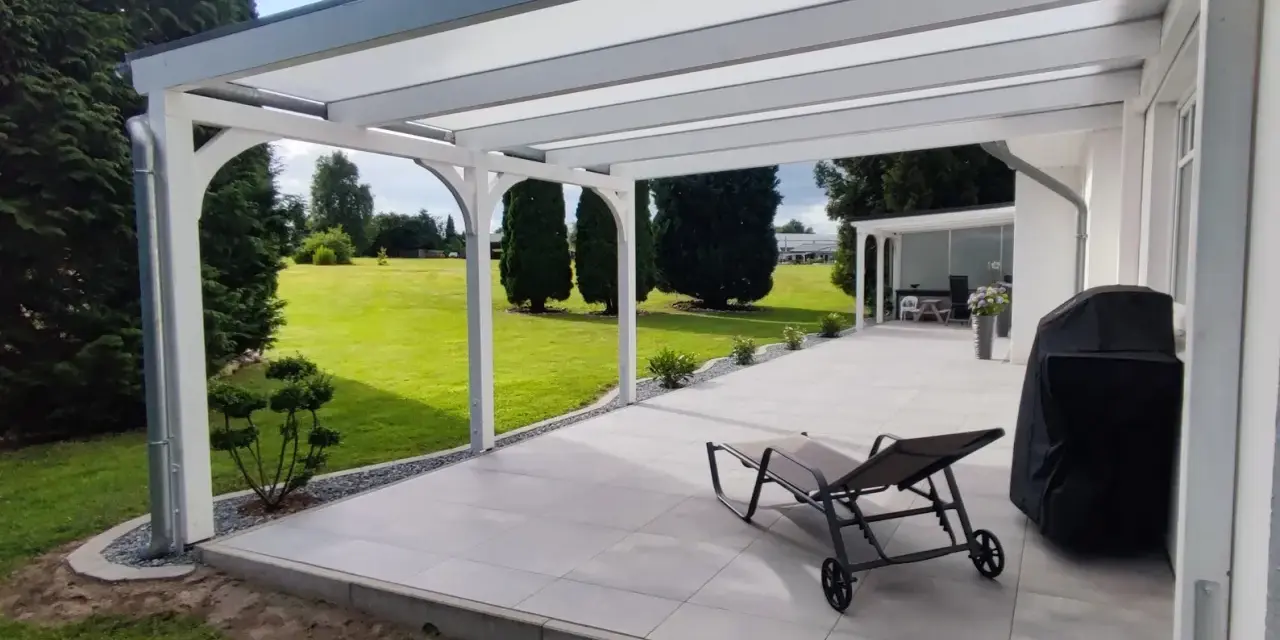 Moderne Terrasse bauen: Überdachter Sitzbereich mit Liegestuhl, Grill und Blick ins Grüne.