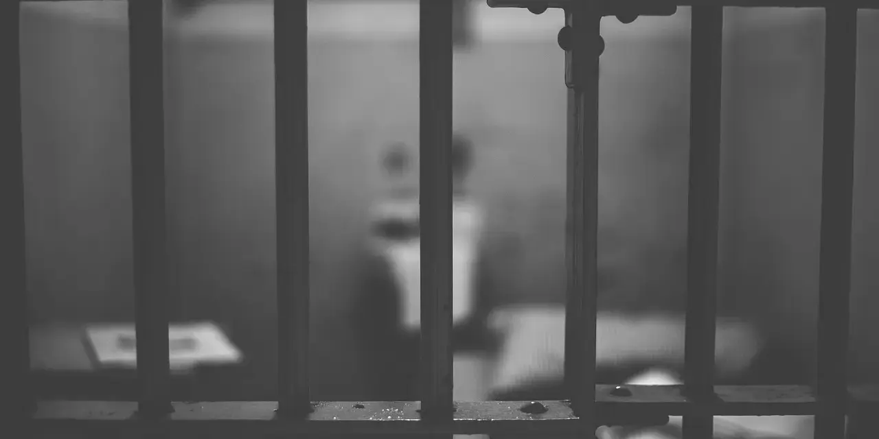 Widok przez kraty więzienne. W tle niewyraźna postać, symbolizująca nadzieję na wcześniejsze zatarcie skazania i nowe życie.