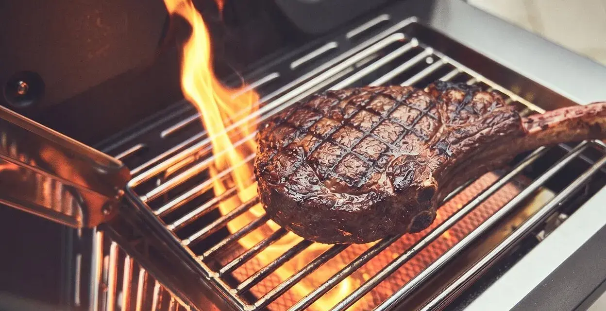 Ein saftiges Steak wird auf einem Gasgrill gegrillt, Flammen züngeln empor.