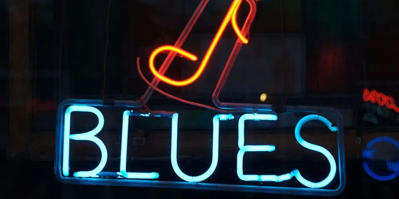Néon bleu lumineux "BLUES" avec une note de musique rouge orangé au-dessus. L'ambiance parfaite pour une soirée blues.