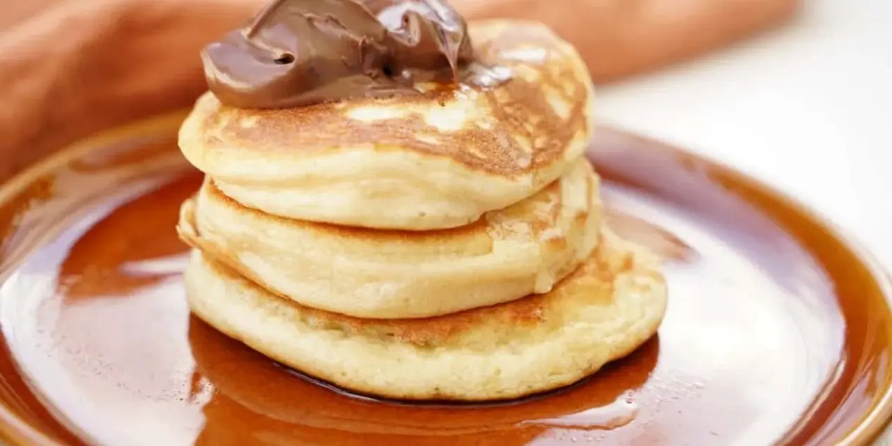 Stack of three fluffy American pancakes topped with chocolate spread on a brown plate.