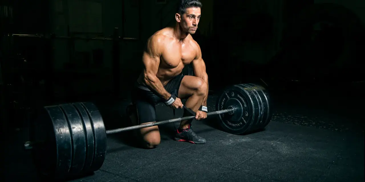 Un homme musclé s'apprête à soulever une barre chargée, profitant d'un temps de repos musculation dans une salle sombre.
