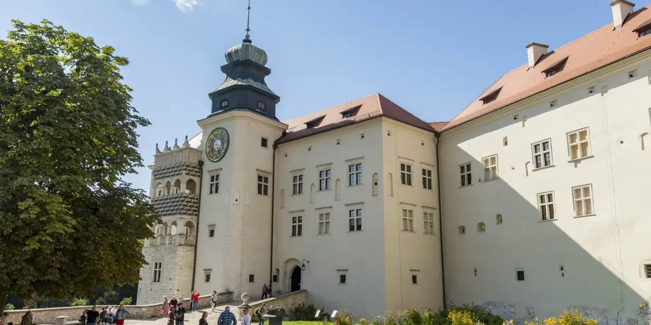 Zamek w Pieskowej Skale z charakterystyczną wieżą zegarową i renesansową attyką. Zwiedzający spacerują po dziedzińcu.
