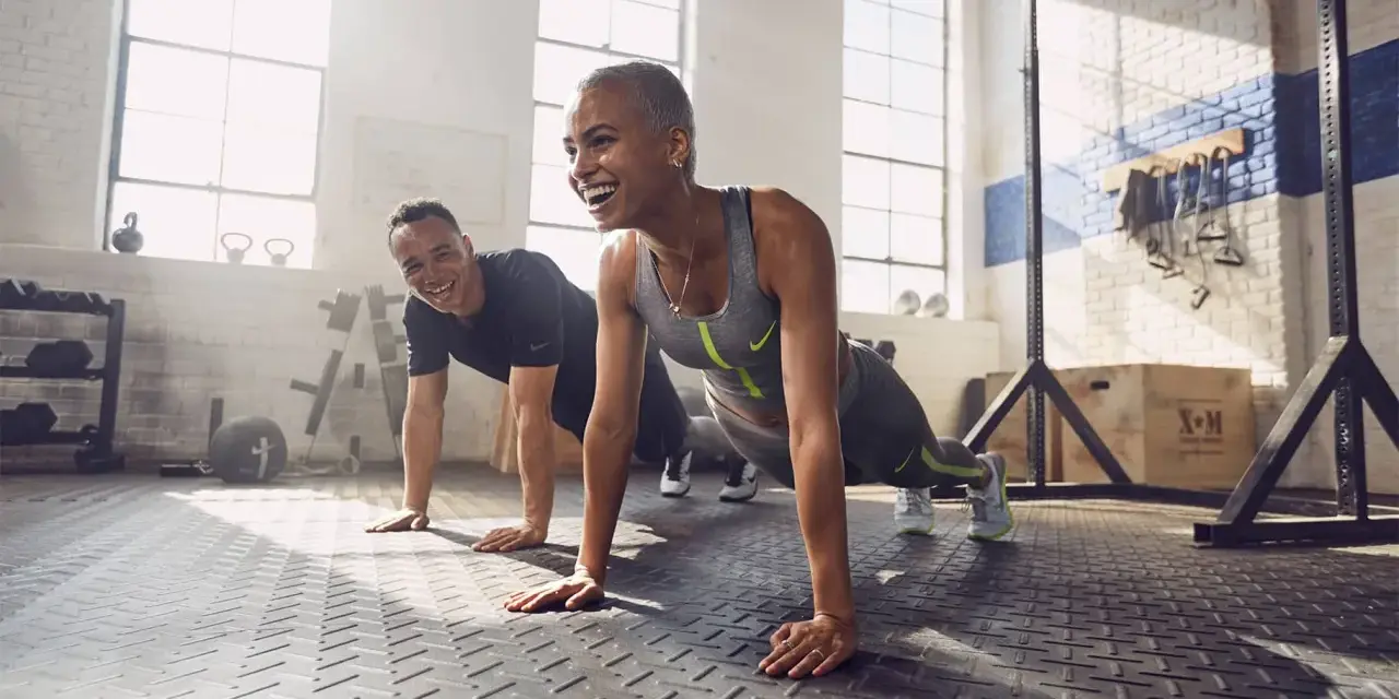 Coppia sorridente in palestra, che fa flessioni. Lo sport è un valido alleato contro la depressione, un modo per ritrovare energia e benessere.
