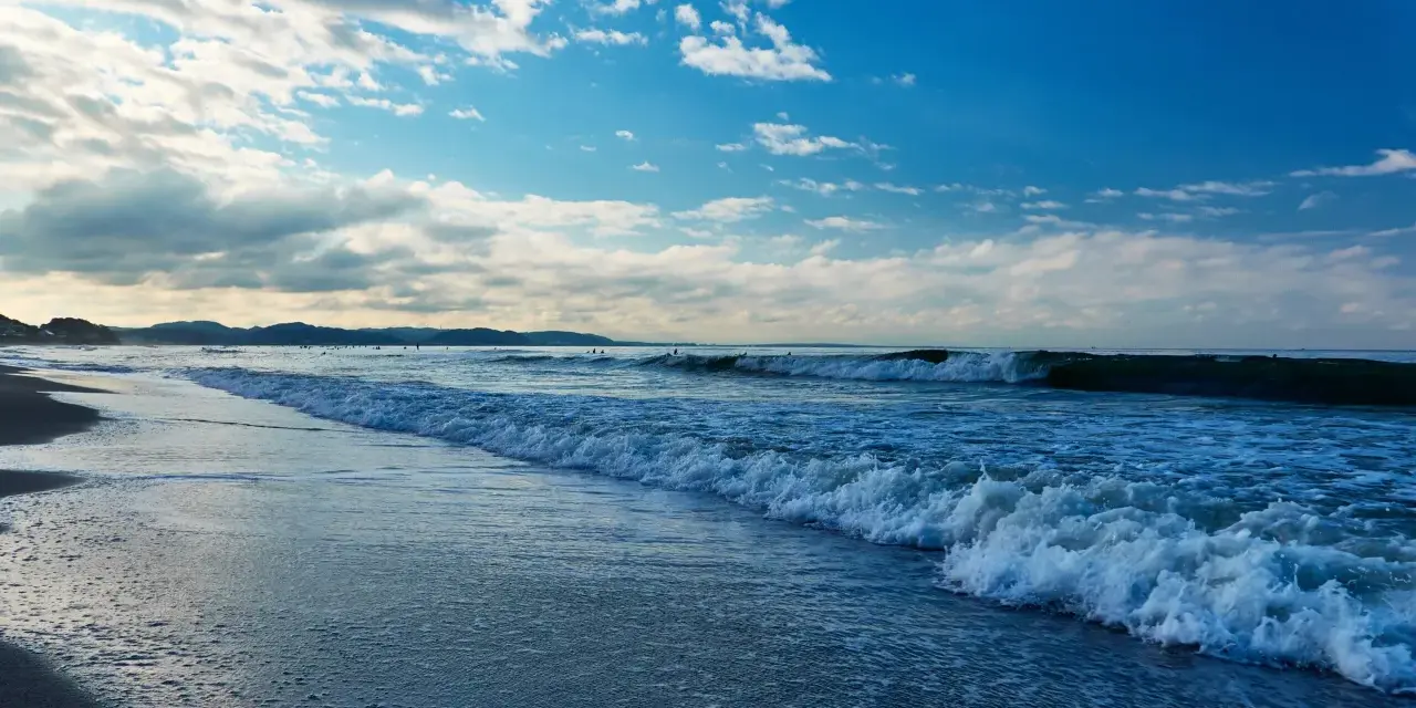 Plaża nad Bałtykiem z falami i błękitnym niebem z chmurami.