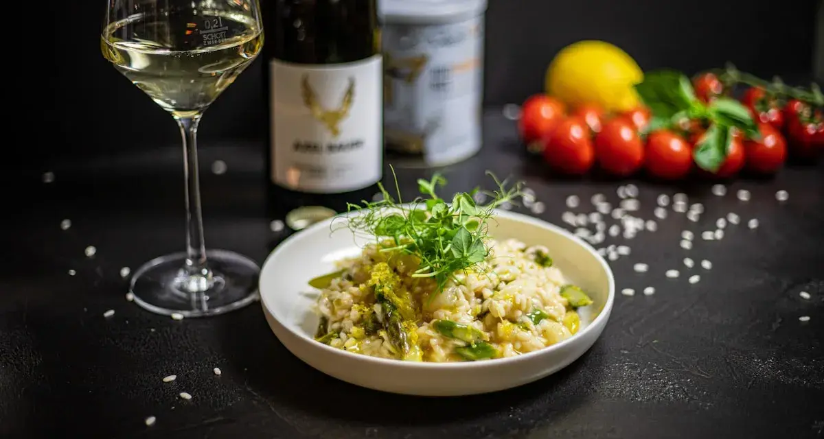 Aksamitne risotto z kurczakiem i szparagami, udekorowane kiełkami. Obok kieliszek białego wina i butelka.