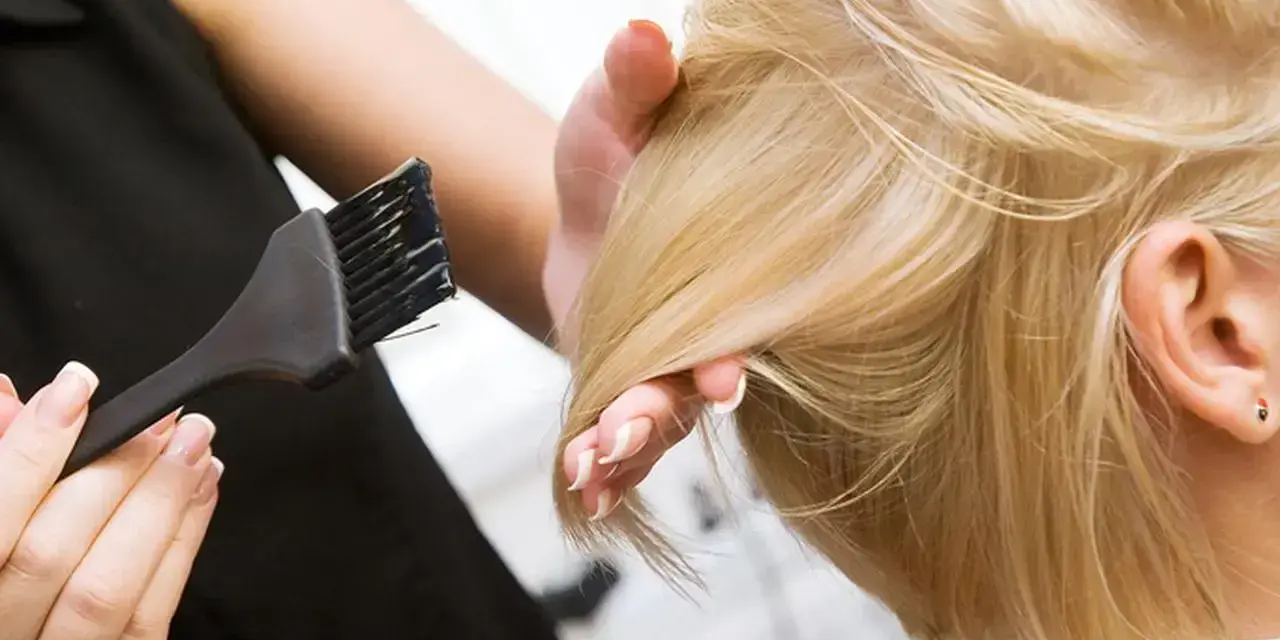 Fryzjerka wykonuje konturowanie włosów blond, nakładając farbę pędzelkiem.