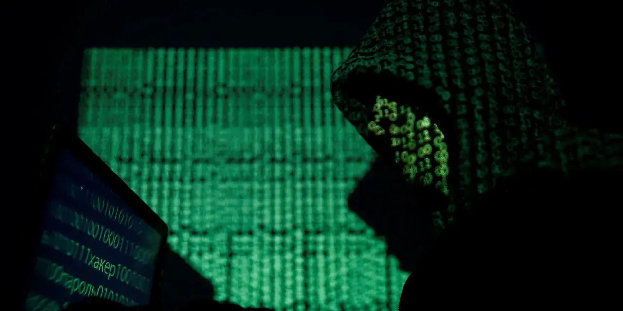 A hooded figure works on a laptop, bathed in the green glow of binary code. This scene evokes the shadowy world of China cyber espionage.