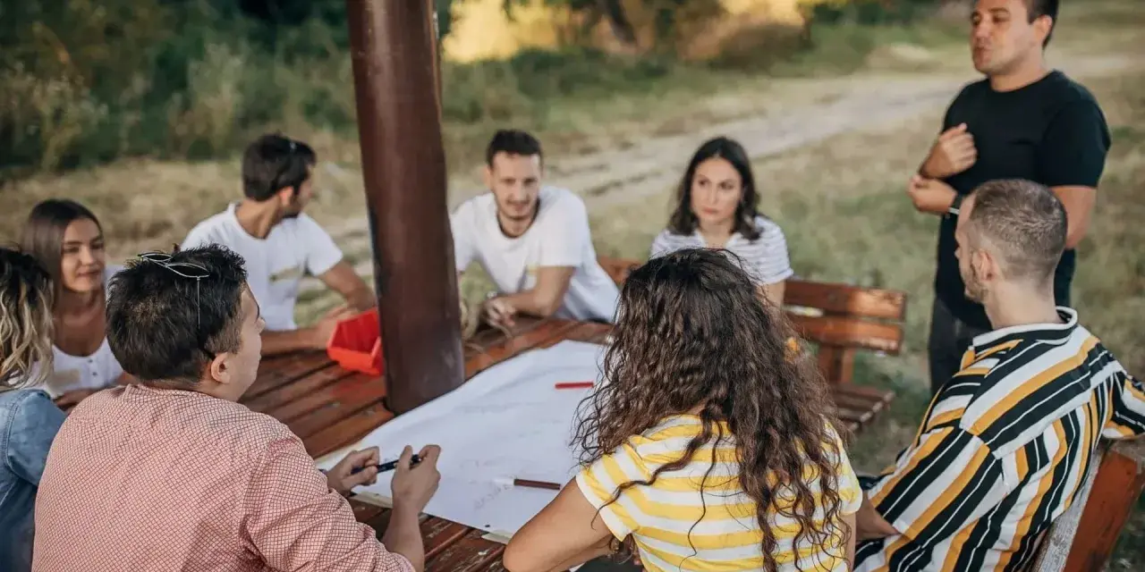 Un groupe discute autour d'une table en bois lors d'une sortie team building en plein air.