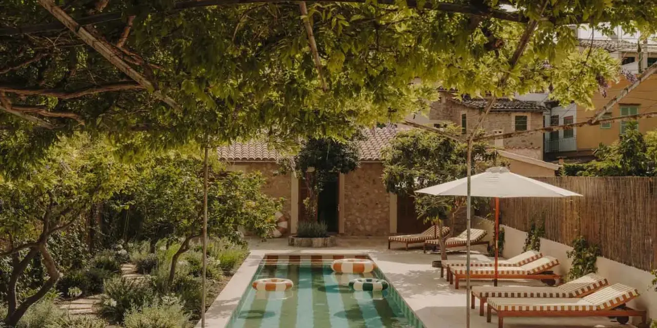 Piscina con galleggianti in un giardino rigoglioso, perfetto per idee piccoli giardini con piscina. Lettini e ombrellone invitano al relax.