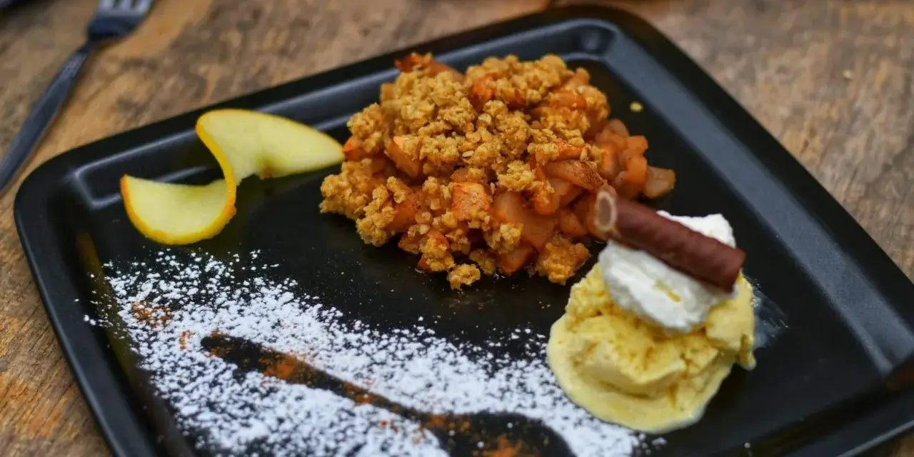 Ein köstlicher Apfel Crumble mit Haferflocken, serviert mit Vanilleeis, Sahne und einem Schokostäbchen.