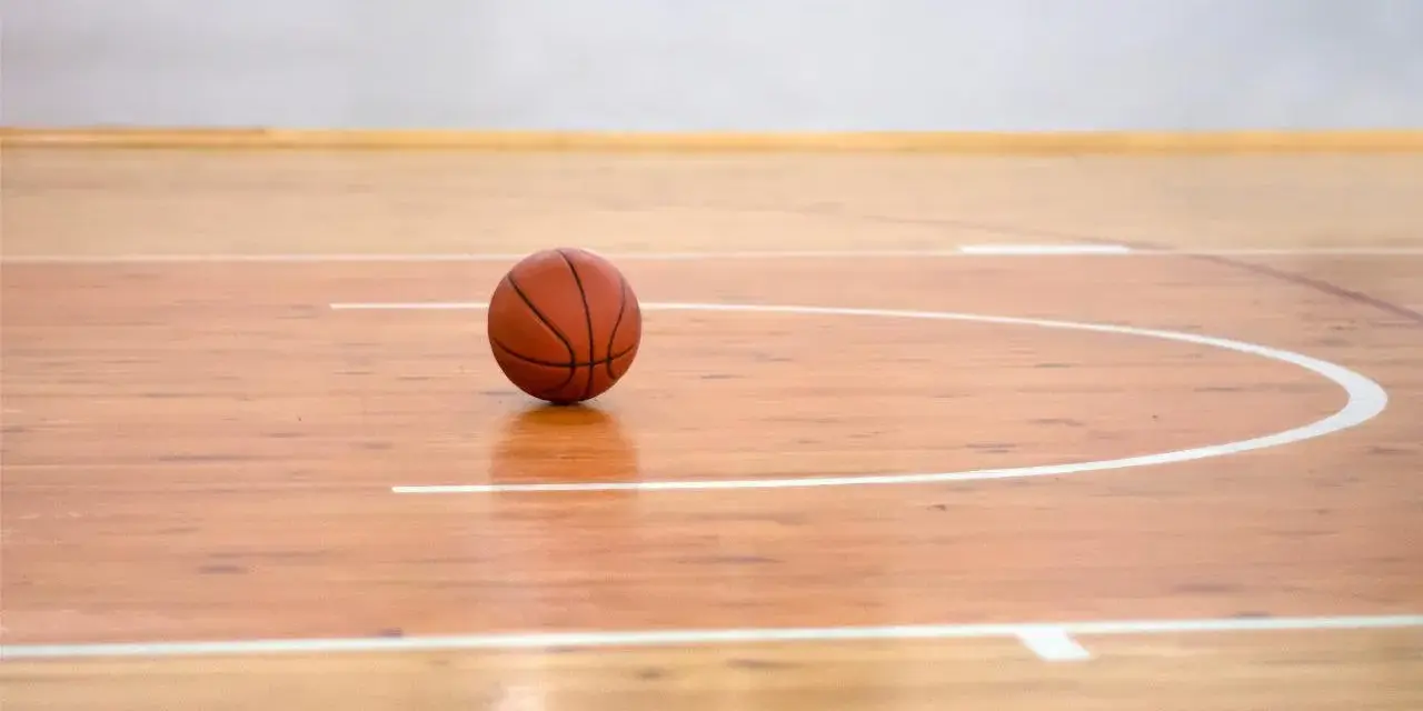 Balón de baloncesto sobre los pavimentos deportivos de madera pulida, listo para el juego.