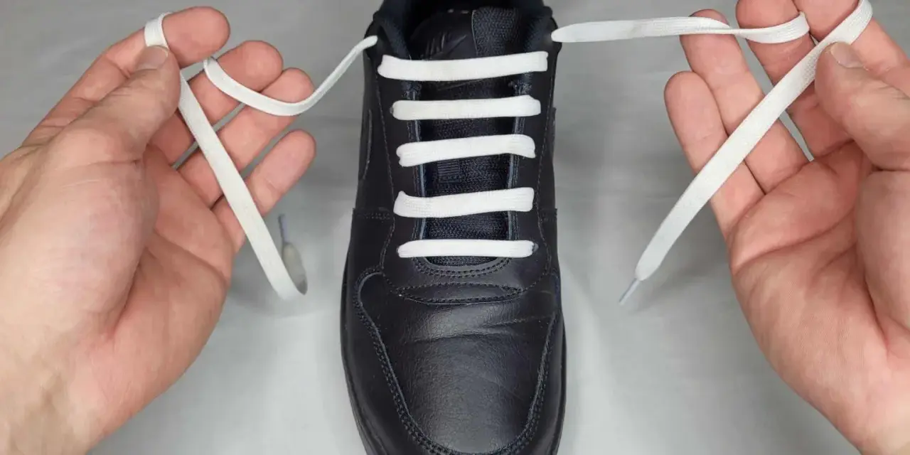 Mani che mostrano come mettere i lacci alle scarpe senza fiocco, con un laccio bianco che attraversa gli occhielli di una scarpa nera.