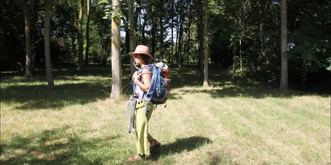 Une randonneuse avec un sac à dos et une poche à eau visible. Elle est dans une forêt, prête pour son aventure.