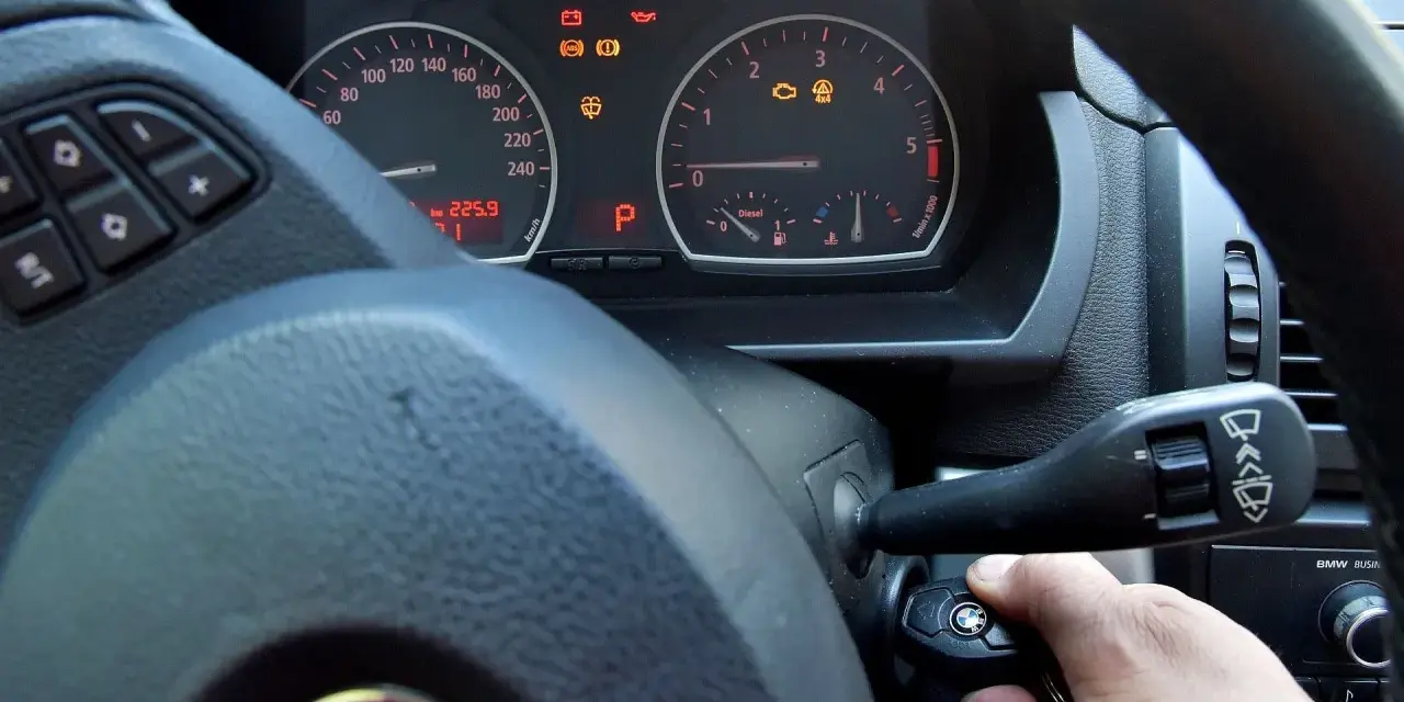 Ręka wsuwa kluczyk do stacyjki, by dowiedzieć się, jak odpalic auto. Na desce rozdzielczej świecą kontrolki.