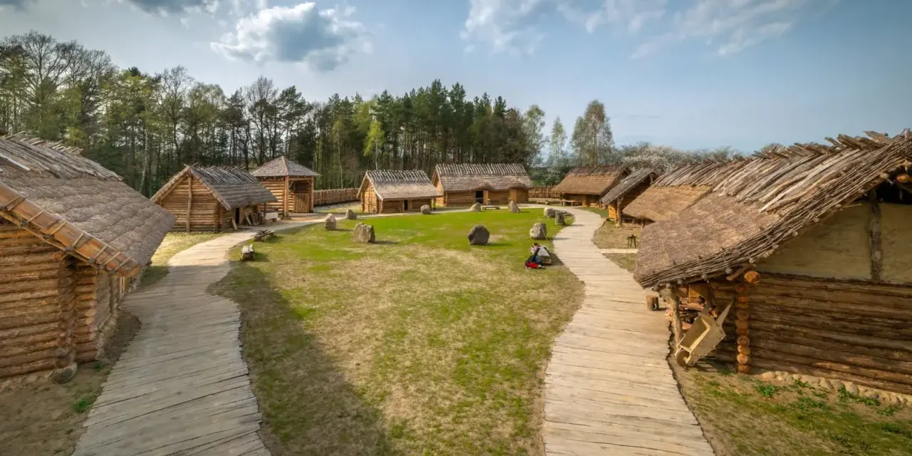 Drewniana osada średniowieczna Sławutowo z chatami krytymi strzechą, kamieniami i ścieżkami.