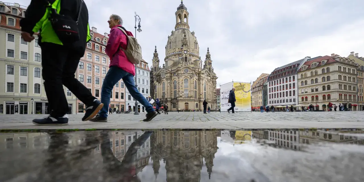 Menschen spazieren über einen nassen Platz vor der Frauenkirche, ein Symbol für offene Kirchen.