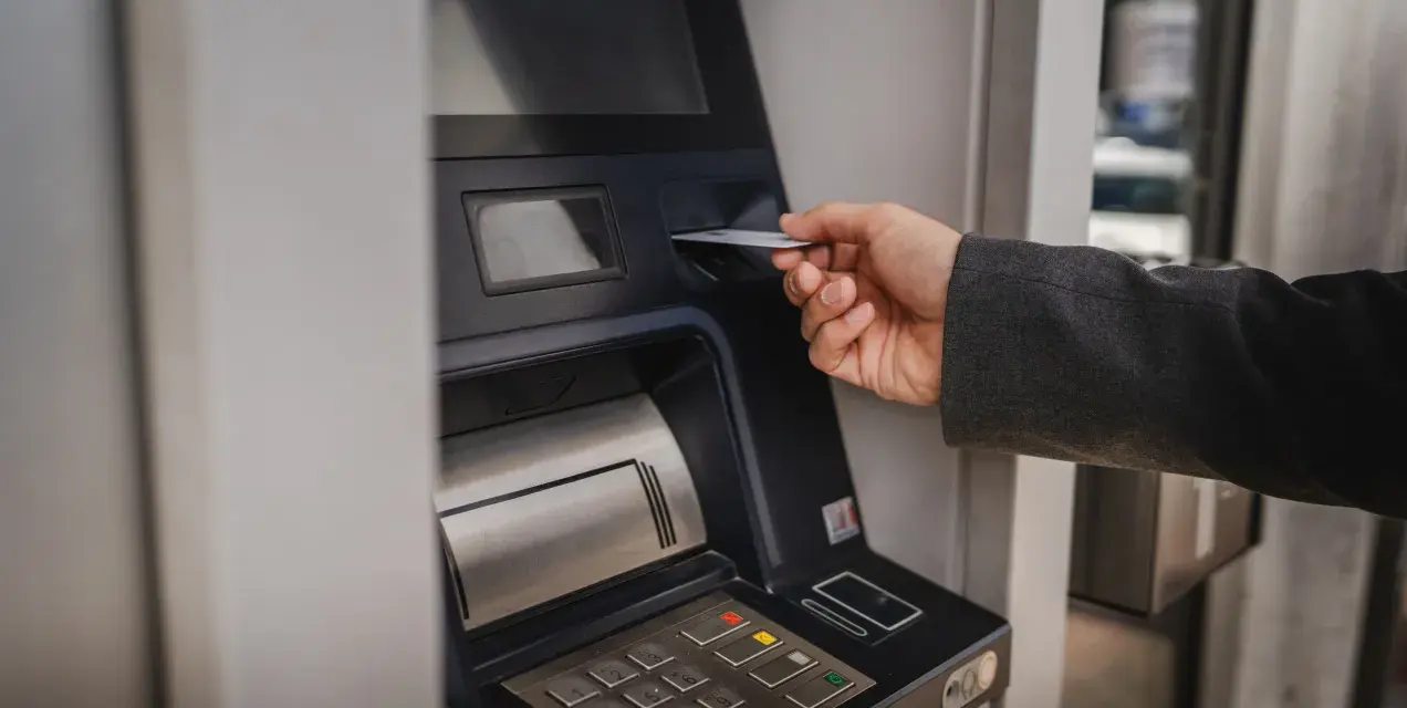 Dłoń wsuwa kartę do bankomatu, by sprawdzić, ile można wypłacić.