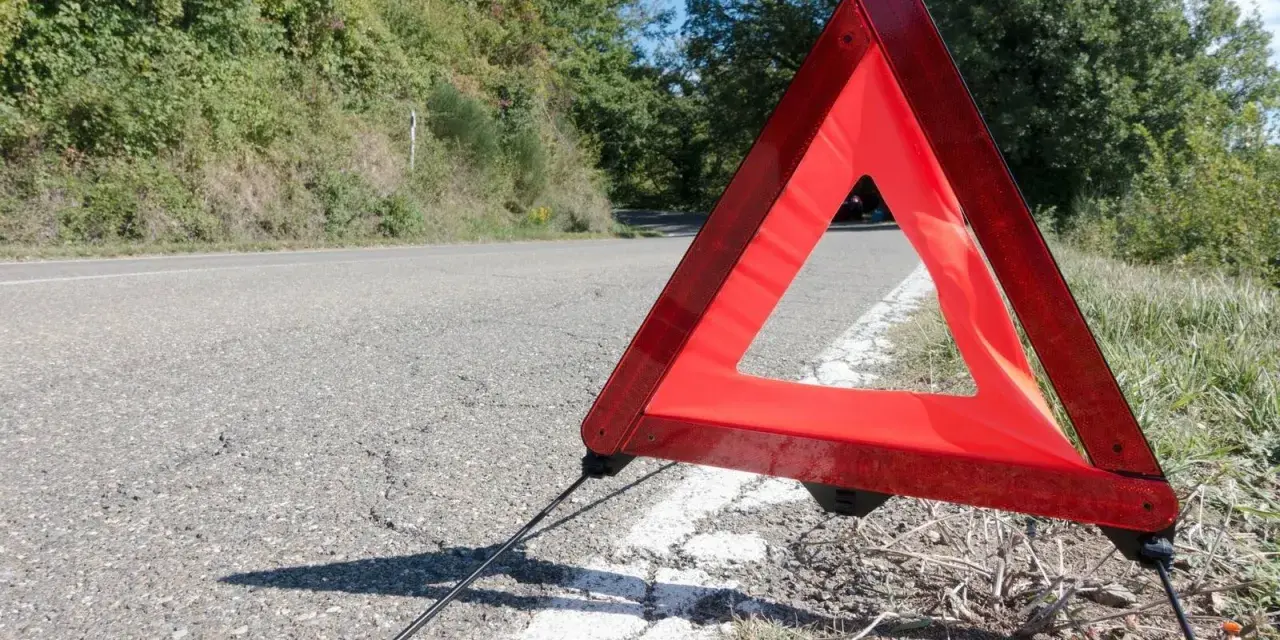 Czerwony trójkąt ostrzegawczy odległości stoi na poboczu drogi, sygnalizując awarię.