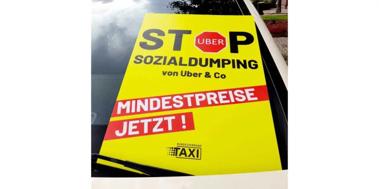 Gelbes Schild auf Taxidach: "STOP SOCIAL DUMPING von Uber & Co. MINDESTPREISE JETZT!". Fordert faire taksi fiyatları.