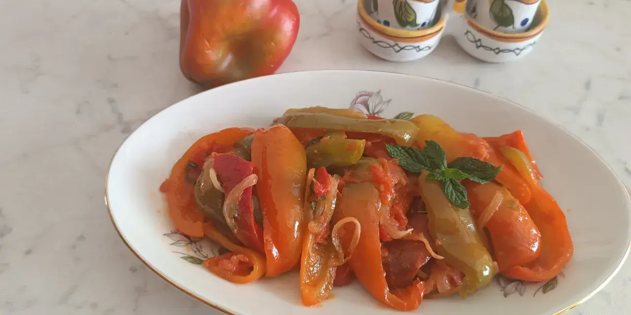 Piatto di peperoni alla siciliana, colorati e saporiti, con un peperone crudo sullo sfondo e saliere decorate.
