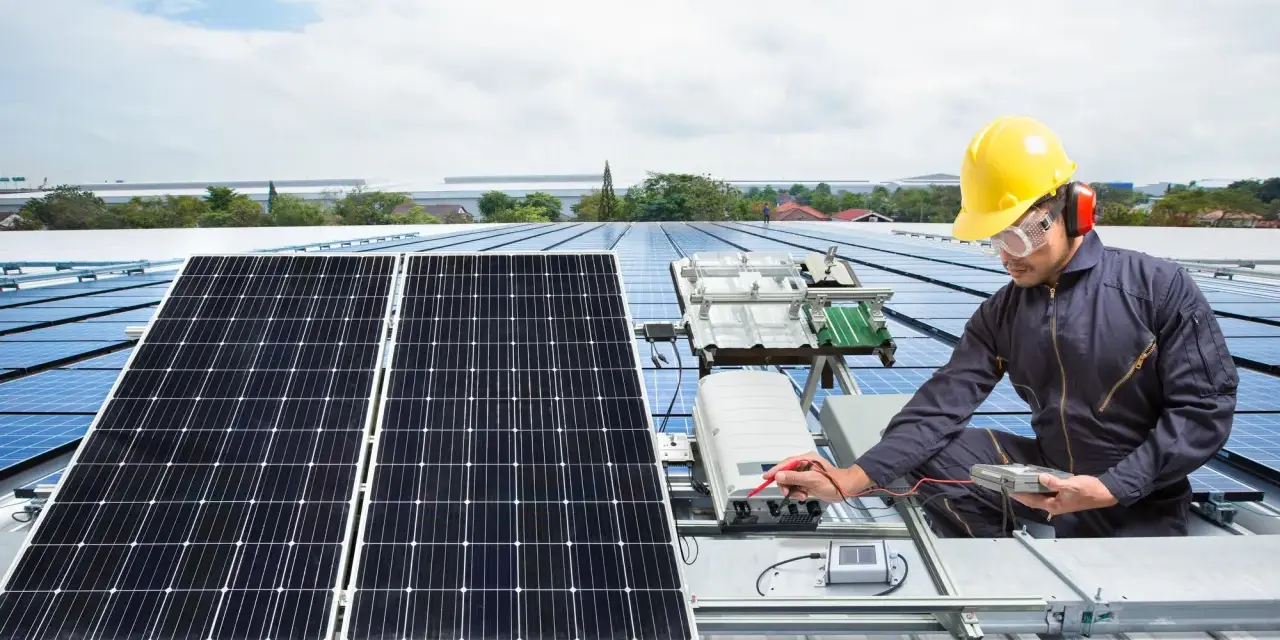 Technik w żółtym kasku sprawdza instalację solar edge na dachu. Panele słoneczne błyszczą w słońcu.