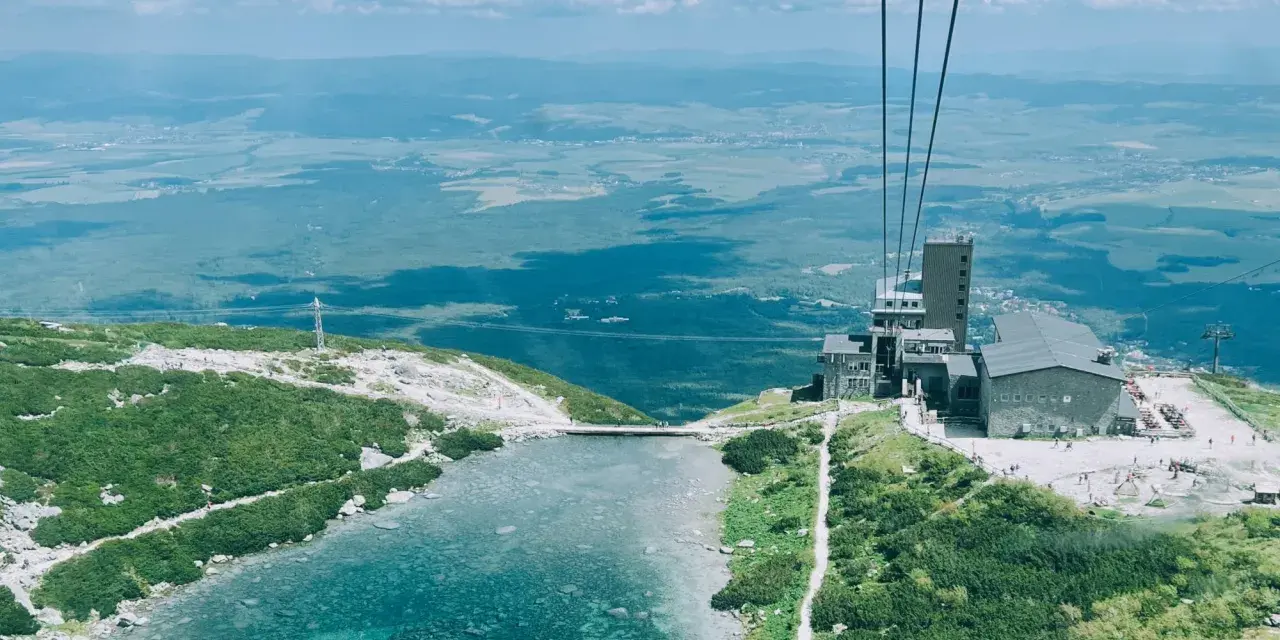 Widok z kolejki linowej na Skalnate Pleso, drugi szczyt w Tatrach. Jezioro, budynek i rozległa panorama.